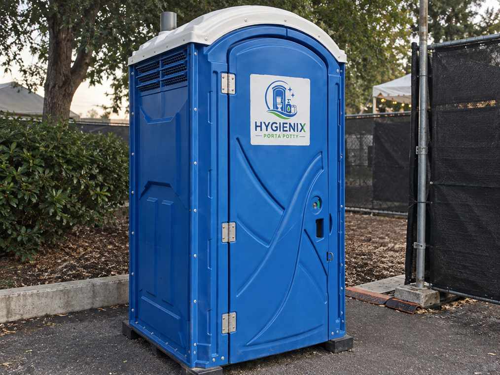 A blue Hygienix Porta Potty unit beside a hedge and fence