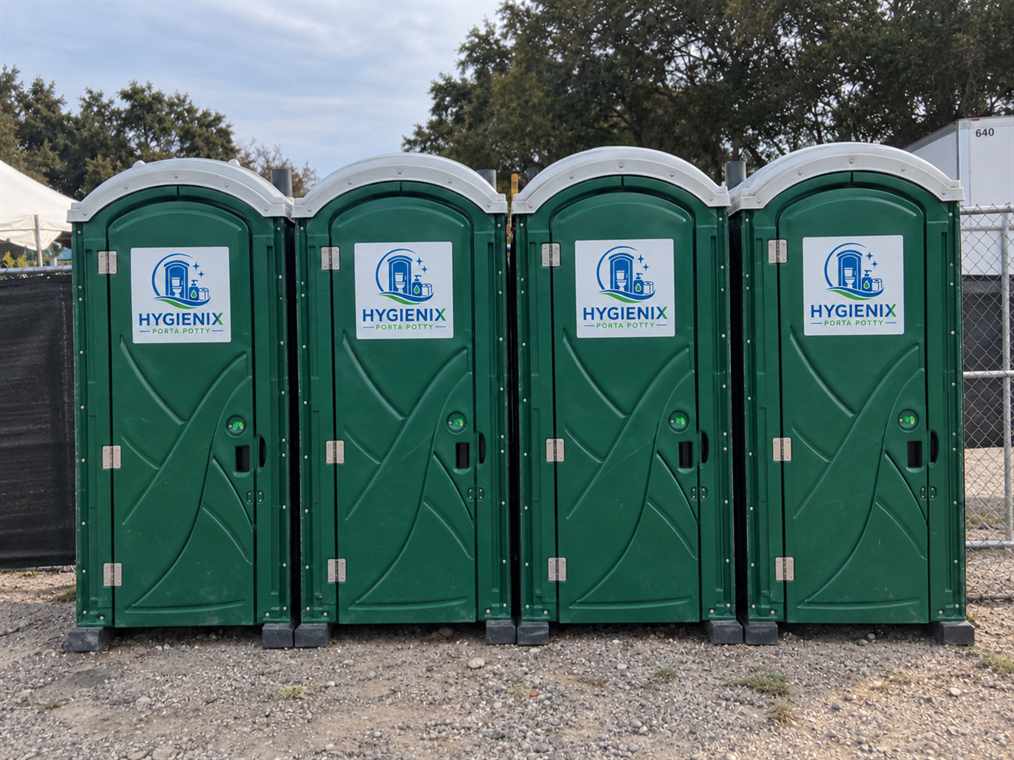 Row of four green Hygienix Porta Potty units on gravel
