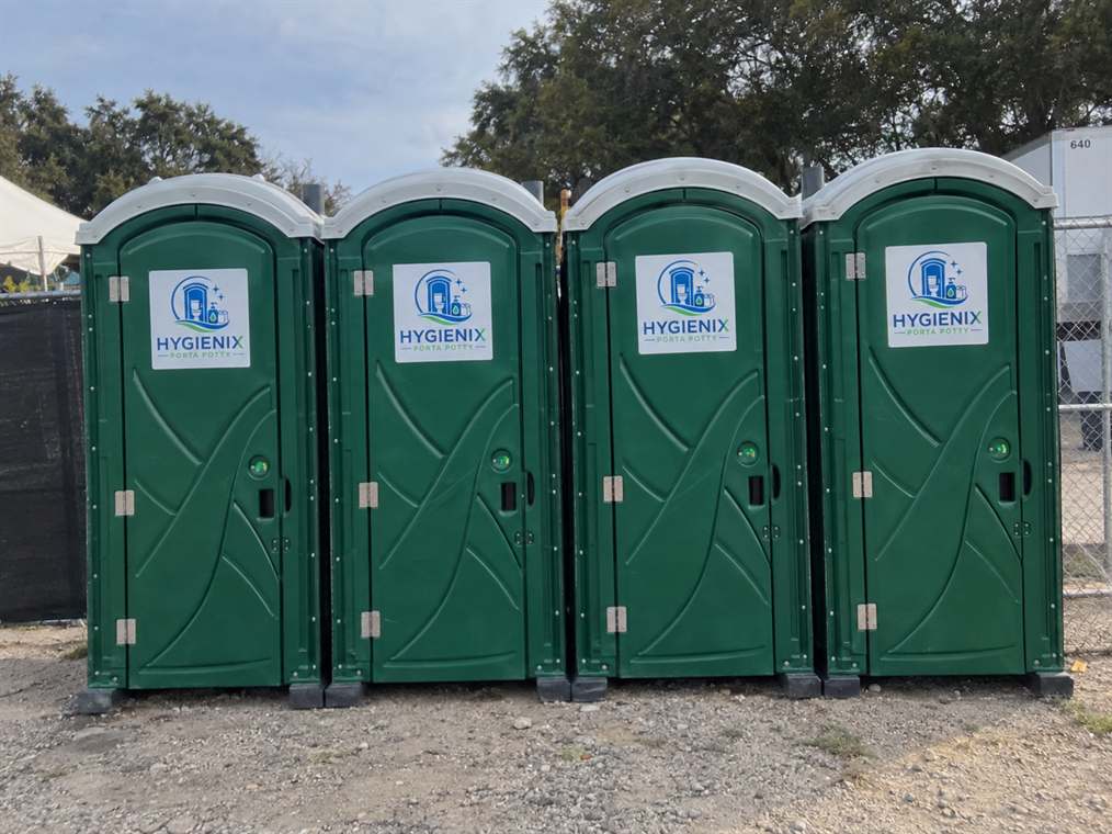 A row of four green Hygienix Porta Potty units against a dark fence