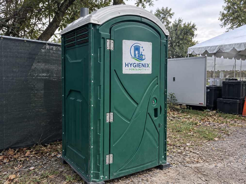 A green Hygienix Porta Potty beside an event tent and trailer
